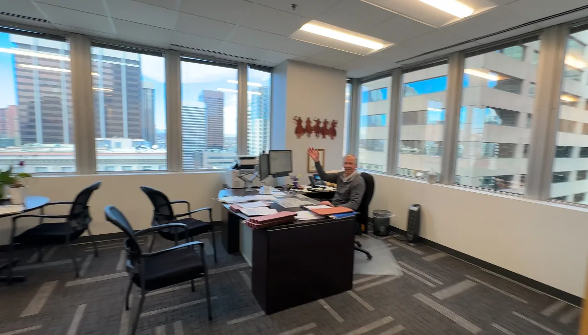 Dan Mahoney waving from his desk in his downtown Denver corner office